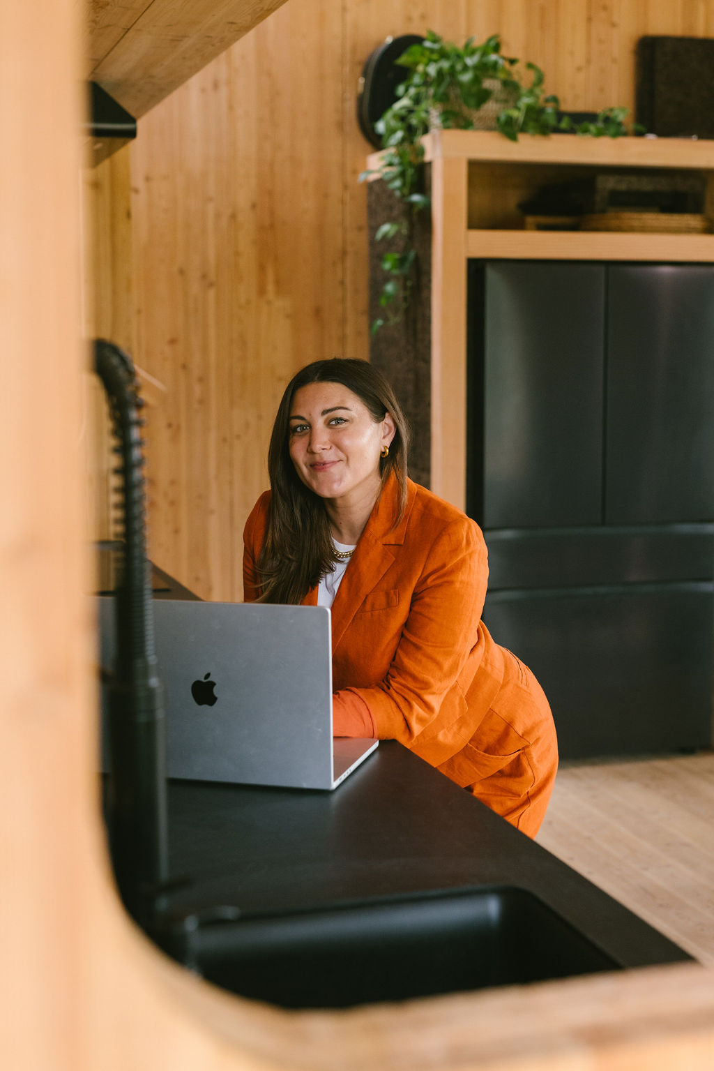 Shana Rehwald stands in an orange suit behind her laptop.